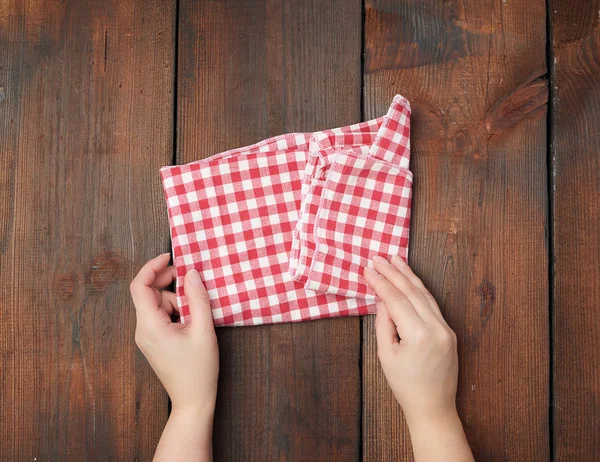 Handen houden wit rood geruite keukendoek op een bruine houten b — Stockfoto