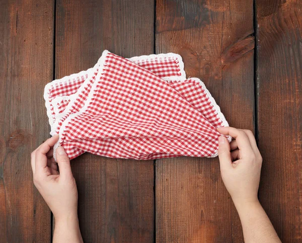 Handen houden wit rood geruite keukendoek op een bruine houten b — Stockfoto