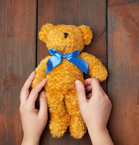 Vrouwelijke handen houden een klein speelgoed teddybeer op een bruine houten rug — Stockfoto