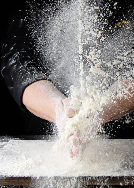 Chef em preto uniforme polvilha farinha de trigo branco em d diferente — Fotografia de Stock