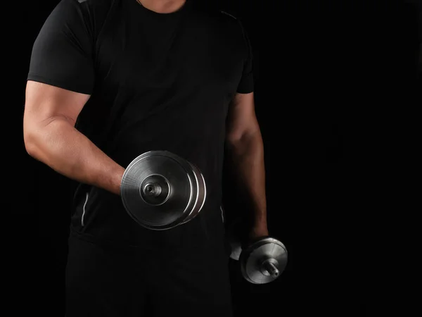 Hombre con ropa negra sostiene pesas de acero en sus manos, su mus — Foto de Stock