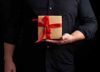 Siyah gömlekli yetişkin bir adam elinde kare kahverengi bir kutu tutuyor.