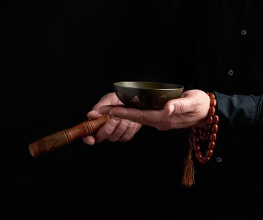 Siyah gömlekli bir adam bakır bir Tibe 'nin etrafında tahta bir sopa çeviriyor.