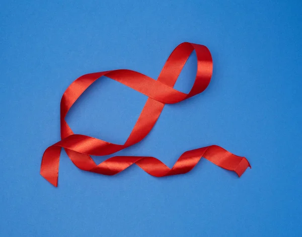 Red silk thin ribbon twisted on a blue background — Stok Foto