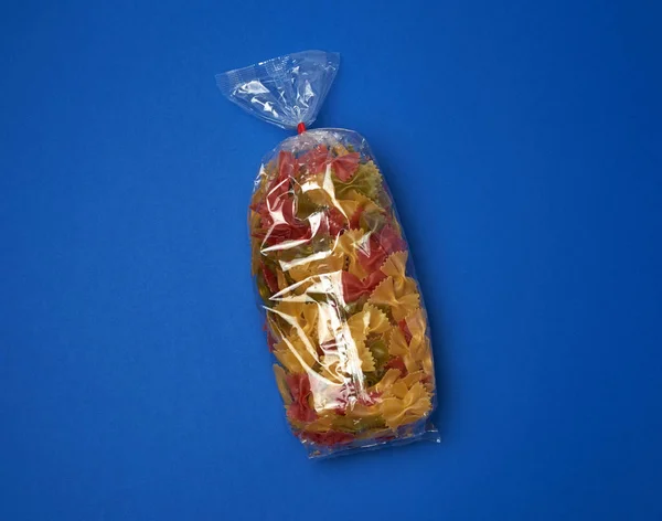 Sac en cellophane transparent avec des pâtes colorées crues sous la forme o — Photo