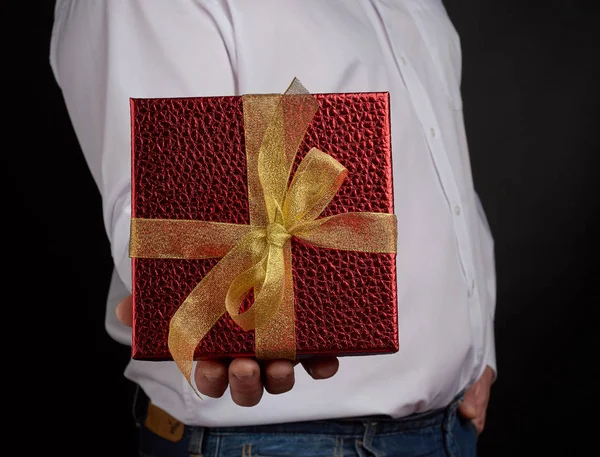 Homme adulte dans une chemise blanche tient une boîte carrée rouge avec un nœud — Photo