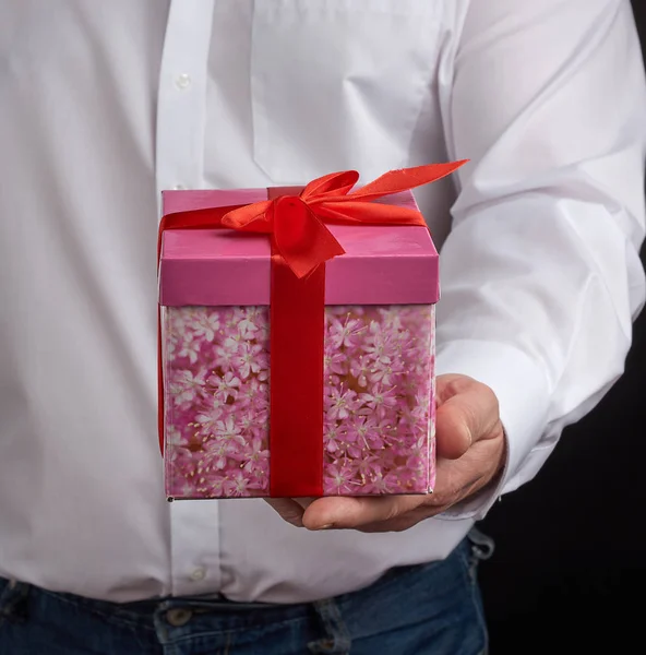 Homme adulte dans une chemise blanche tient une boîte en carton cadeau rose avec — Photo