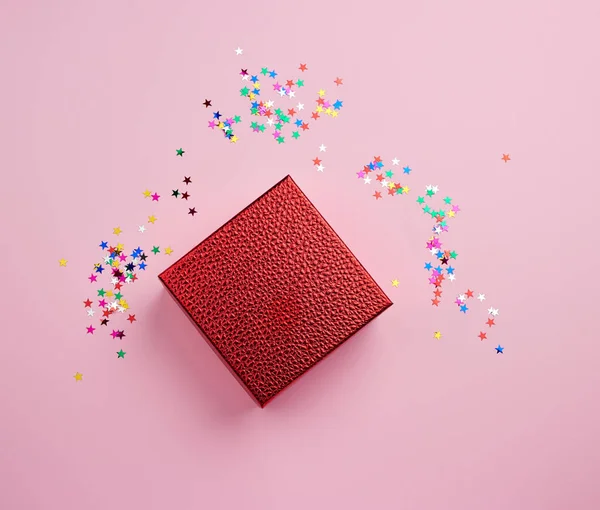 Cuadrado rojo brillante caja y destellos multicolores en un fondo rosa — Foto de Stock