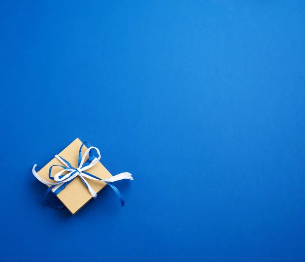 Bruin kartonnen geschenkdoosje, strikken op een blauwe achtergrond — Stockfoto