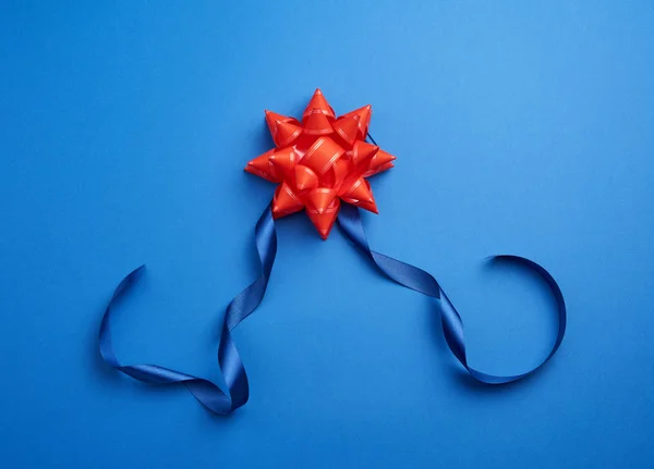 Sutra biru tipis pita memutar dan merah berkilau busur pada backgr biru — Stok Foto