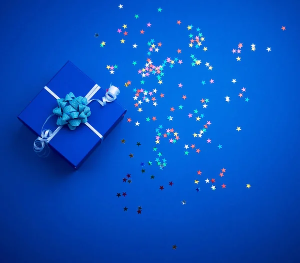 Cuadrado azul brillante caja con un arco y destellos multicolores en un — Foto de Stock