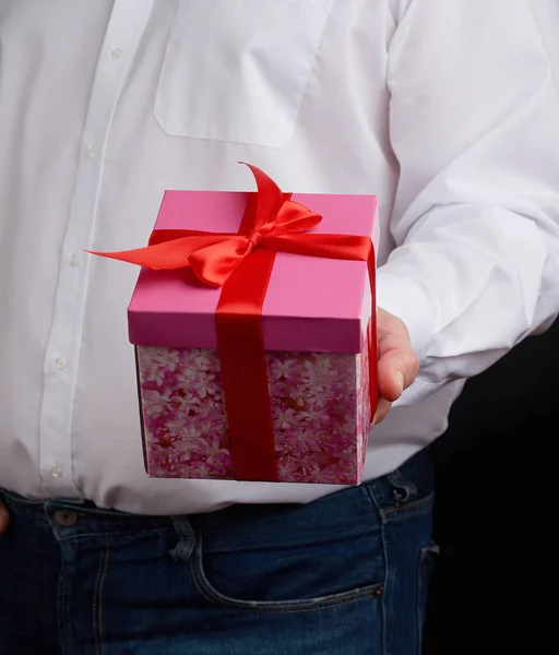 Homme adulte dans une chemise blanche tient une boîte en carton cadeau rose avec — Photo