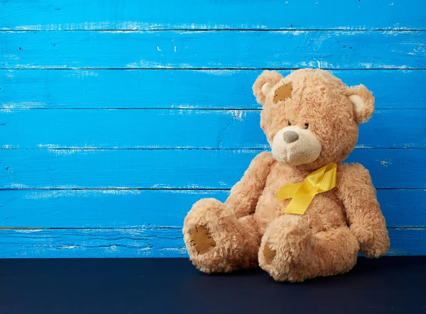 Medvídek hnědý sedí a žlutá hedvábná stuha na modrém dřevě — Stock fotografie