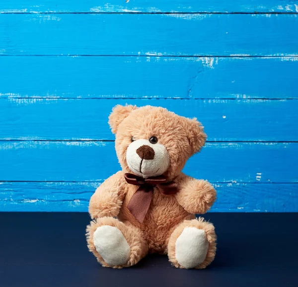 Urso de pelúcia bege sentado em um fundo de madeira azul — Fotografia de Stock