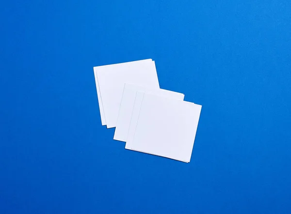 Prázdné bílé malé čtvercové listy papíru na modrém pozadí — Stock fotografie
