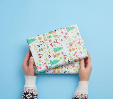 İki kadın eli mavi arka planda kapalı bir kutu tutuyor.