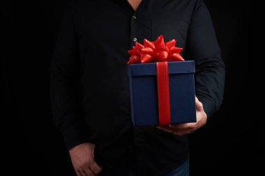 Siyah tişörtlü yetişkin bir adam elinde kırmızı boncuklu mavi bir kutu tutuyor.