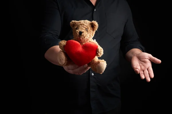 Взрослый мужчина в черной рубашке держит бурого плюшевого медведя с красным h — стоковое фото