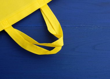 Mavi ahşap arka planda yeniden kullanılabilir sarı yapışkan çanta