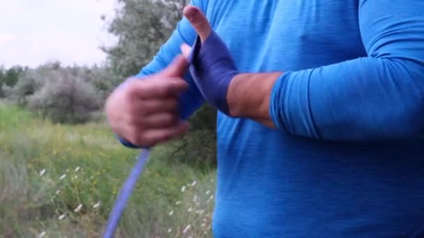 身穿蓝色运动服的体重增加的成年人在公园里用蓝色的纺织品绷带把他的手缩回用于户外运动和拳击 — 图库视频影像