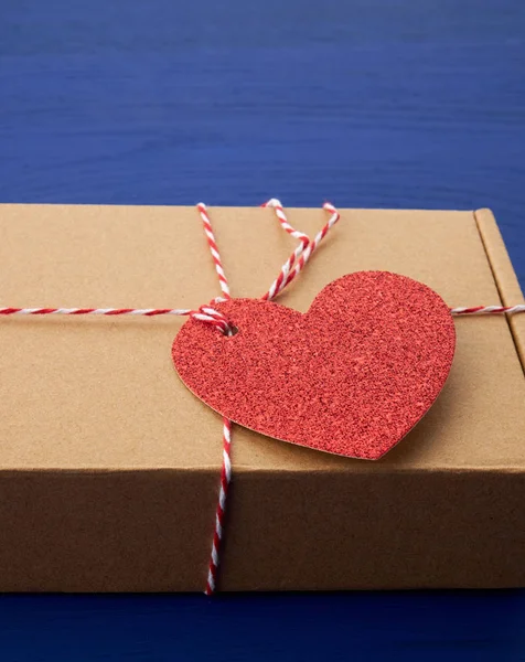 Rectangular brown box with a gift and a red paper heart tied to — 스톡 사진