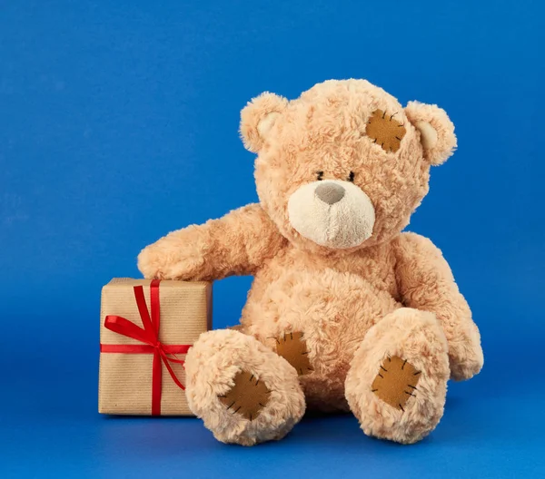 Большой бежевый плюшевый медведь держит коробку, завернутую в коричневую бумагу и ти — стоковое фото