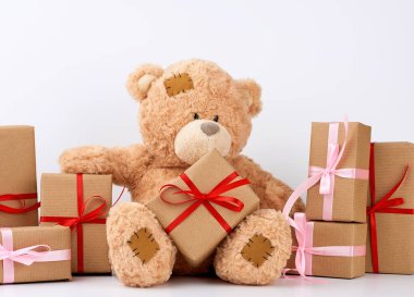 Yamalı büyük bej bir oyuncak ayı, kutuda bir yığın hediye.