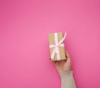 Kadın eli kahverengi bir kutu tutuyor. Pembe bir fiyonk takıyor.