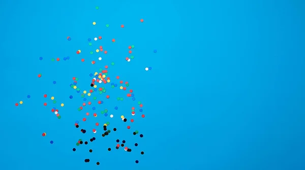 Błyszczące wielokolorowe okrągłe konfetti rozrzucone na niebieskim tle — Zdjęcie stockowe