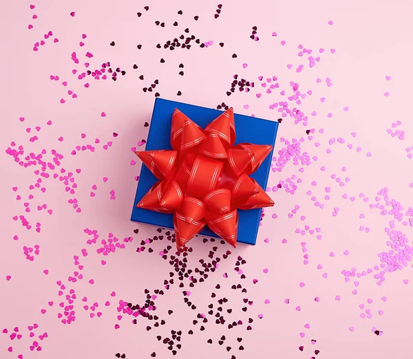 Kotak hadiah biru persegi tertutup dengan busur merah pada latar belakang merah muda — Stok Foto