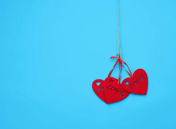 Красные войлочные сердца, висящие на коричневом и синем фоне — стоковое фото