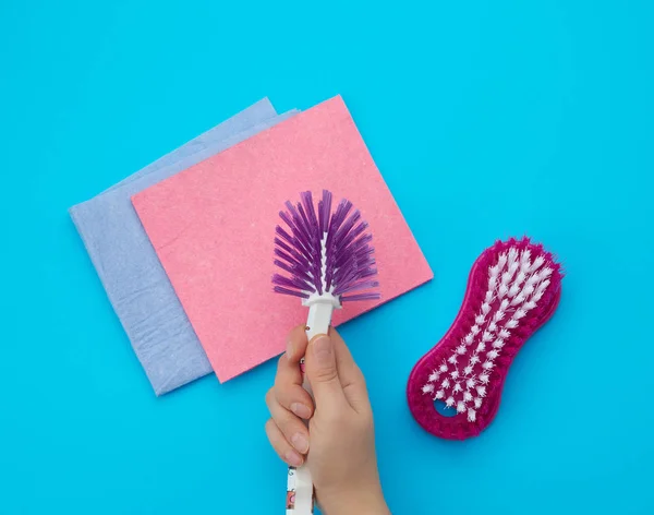 Hand holds a plastic brush for cleaning housework, blue backgrou — Stock Photo, Image