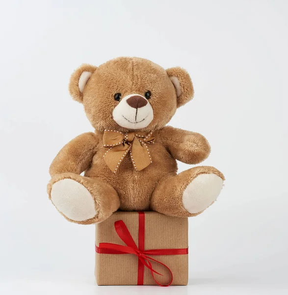 Niedlichen kleinen braunen Teddybär hält eine braune Schachtel mit einem roten Band — Stockfoto