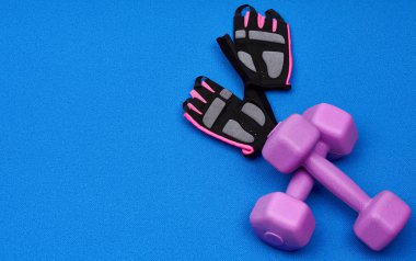 Bir çift mor plastik halterler, mavi neoprene bir paspas üzerinde eldivenler.