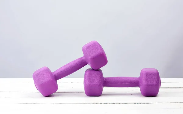 Par de pesas de plástico púrpura para los deportes en una ba de madera blanca — Foto de Stock