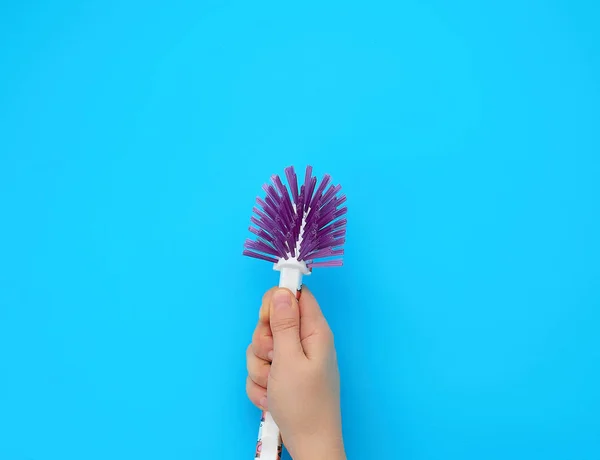 Mano sostiene un cepillo de plástico para la limpieza de las tareas domésticas, fondo azul — Foto de Stock