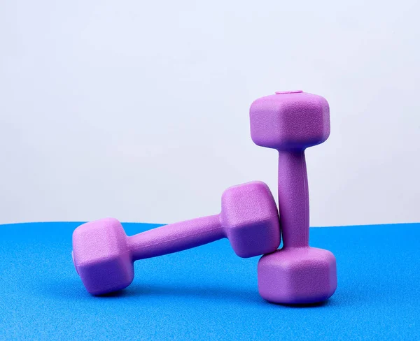 Par de pesas de plástico púrpura en una esterilla de neopreno azul — Foto de Stock