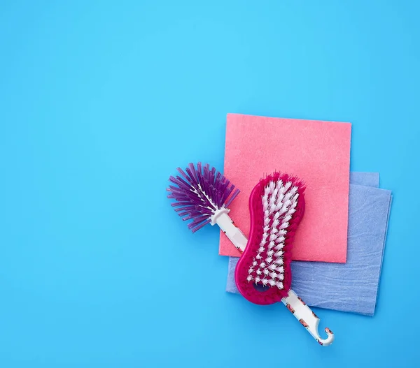 Plastic pink brush and square dishwashing rag on a blue backgrou — Stock Photo, Image