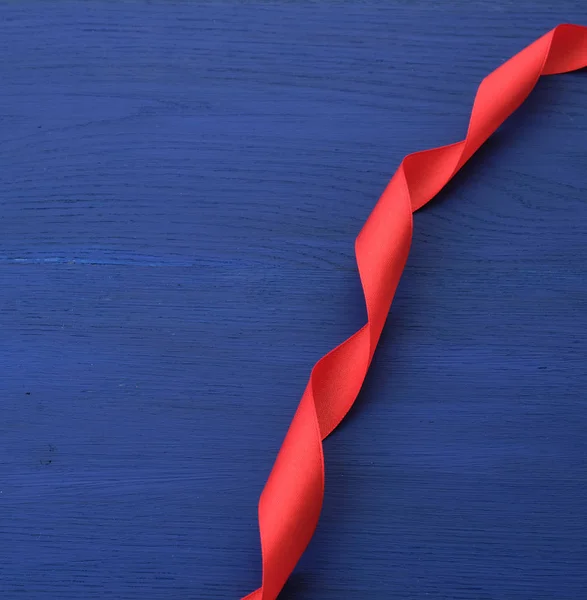 Тонкая красная шелковая лента на голубом деревянном фоне — стоковое фото
