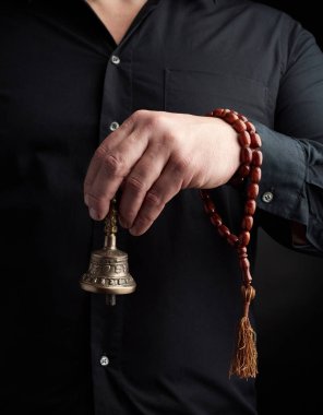 Siyah tişörtlü yetişkin bir adam bakır bir Tibet ayin çanı tutuyor.