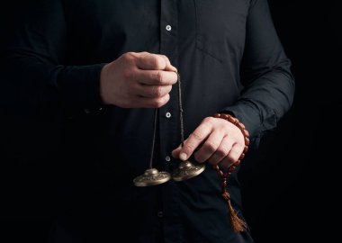 Siyah elbiseli yetişkin adam elinde bir çift bronz K tutuyor.