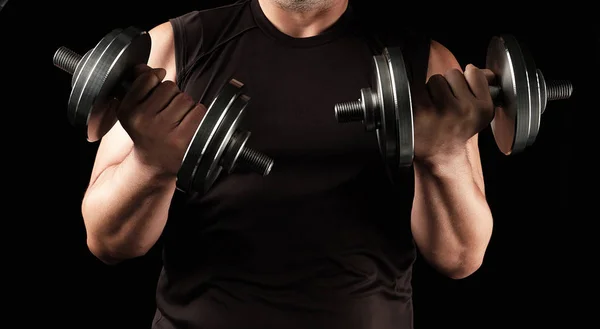 Hombre adulto con ropa negra sostiene pesas de acero en sus manos, h — Foto de Stock