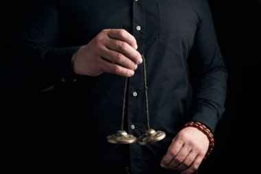 Siyah elbiseli yetişkin adam elinde bir çift bronz K tutuyor.