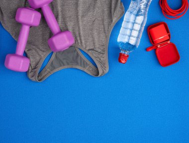 bir çift mor plastik dambıl, gri spor gömlek mavi bir ba üzerinde