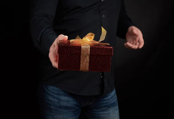 Volwassen man in een zwart shirt houdt een rode vierkante doos met een geknoopte — Stockfoto