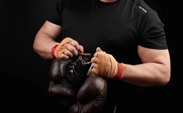 Atleta muscular em um uniforme preto detém boxe marrom muito velho — Fotografia de Stock