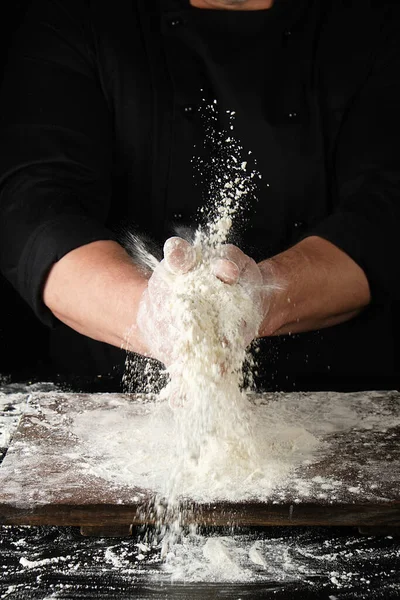 Chef em preto uniforme polvilha farinha de trigo branco em d diferente — Fotografia de Stock