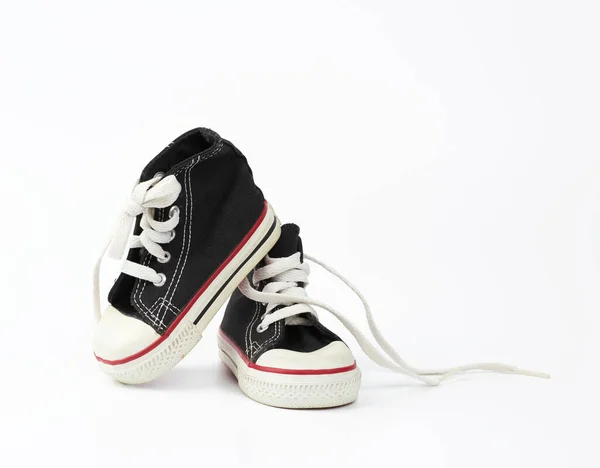 Pair of black textile children's sneakers with white untied shoe — Stock Photo, Image