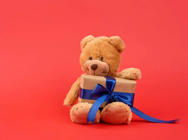 Cute little brown teddy bear holds a brown box with a blue ribbo — Stock Photo, Image