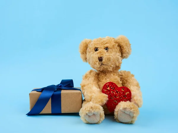 Cute little brown teddy bear holds a brown box with a blue ribbo — Stock Photo, Image